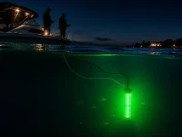 Green underwater fishing light attracting fish beside a boat during night fishing